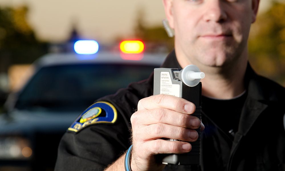 A man is driving a car while holding a bottle of beer.