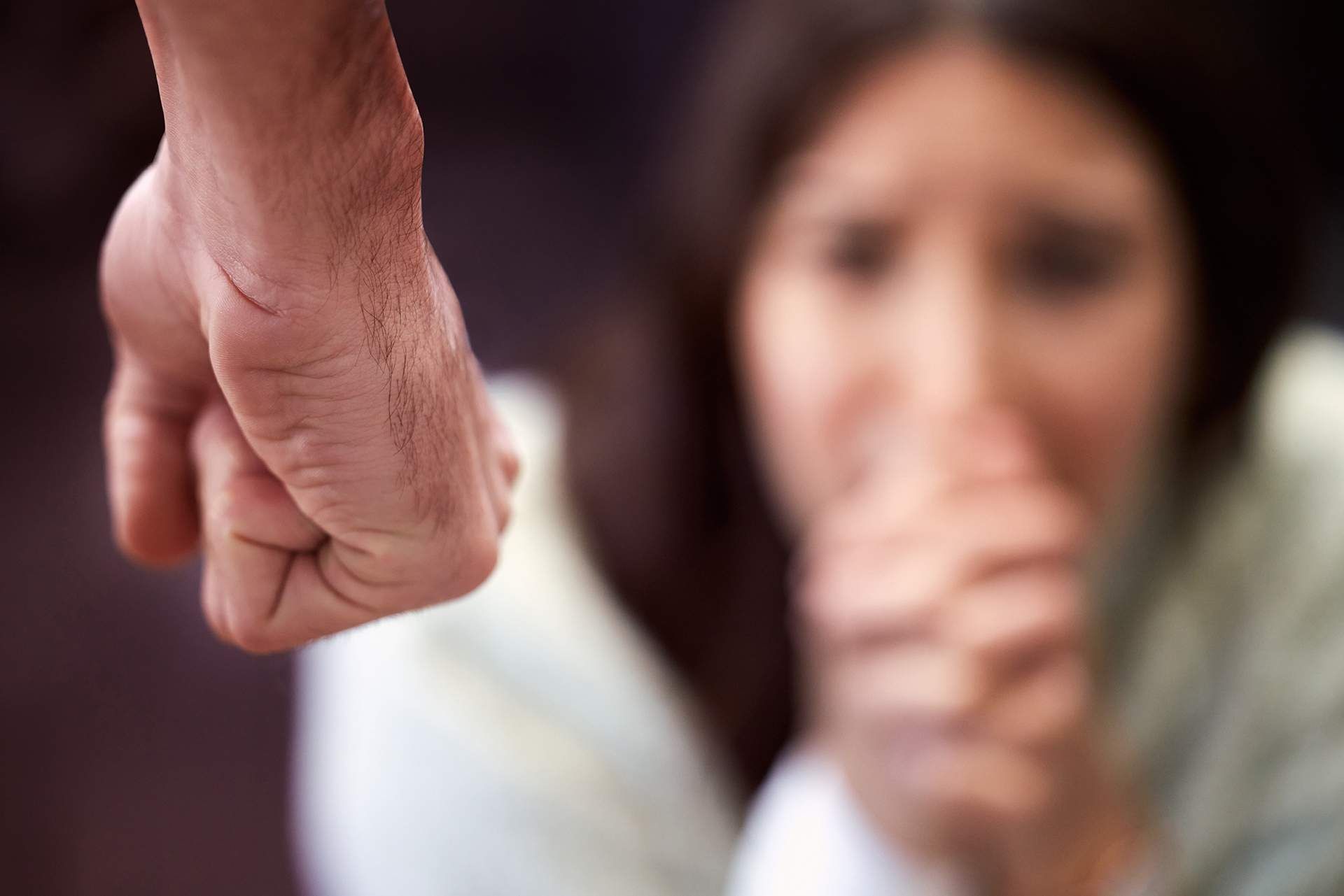 Fist raised towards a blurred, frightened woman covering her mouth.