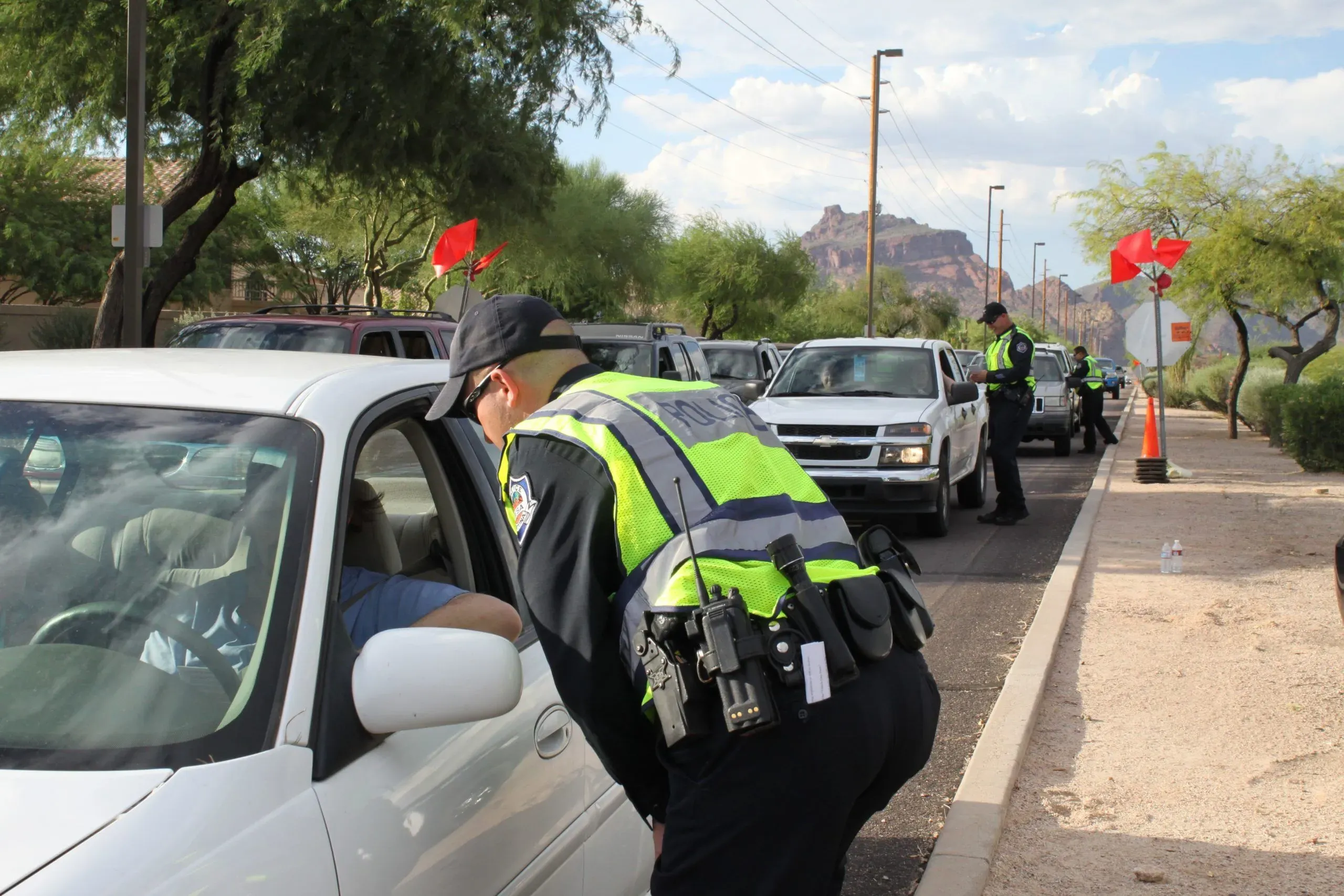 Police officer conducting a DUI checkpoint, interacting with a driver in a white car, surrounded by multiple vehicles and traffic cones, emphasizing DUI enforcement in Texas.
