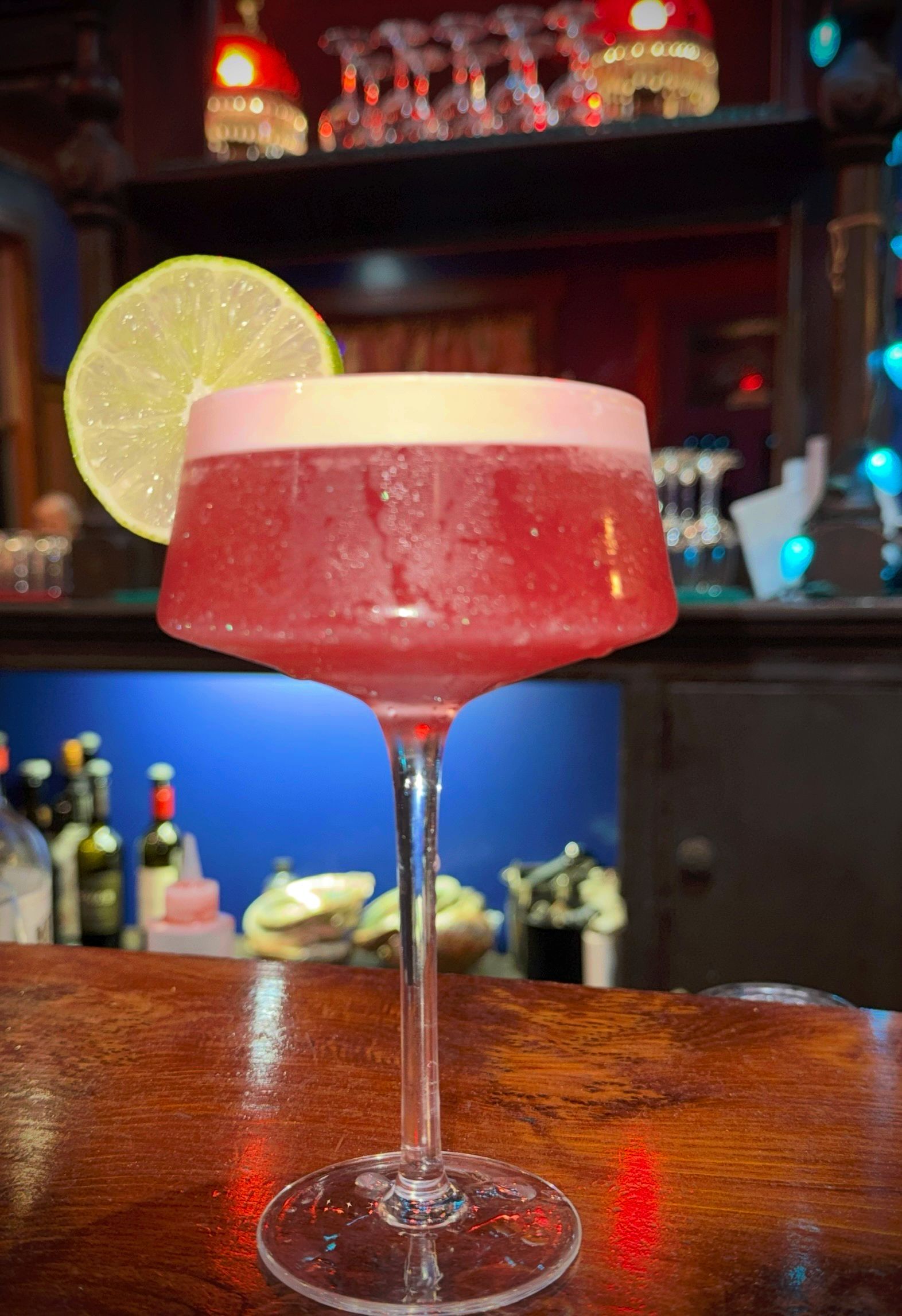 A close up of a red cocktail in a martini glass on a bar.