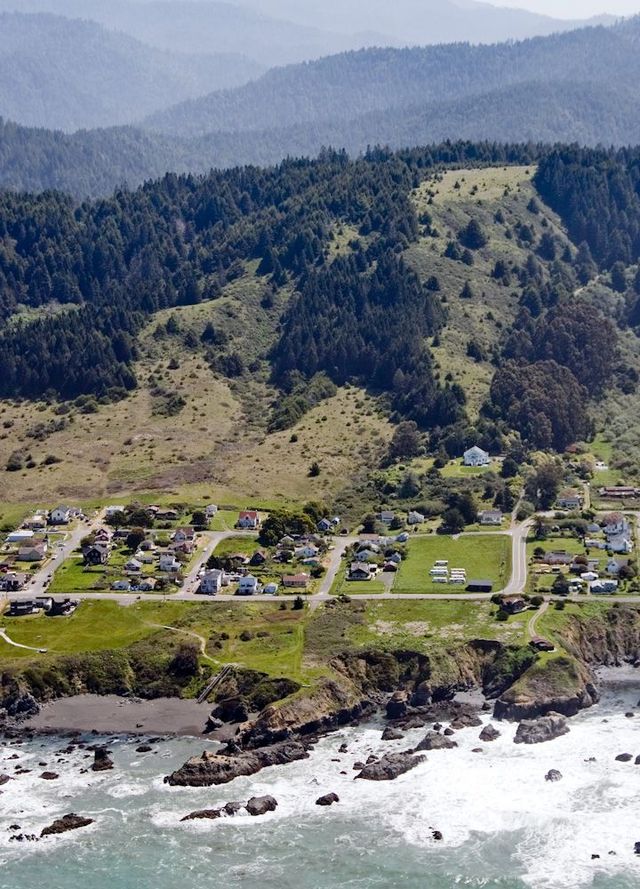 An aerial view of a small town on the coast with mountains in the background