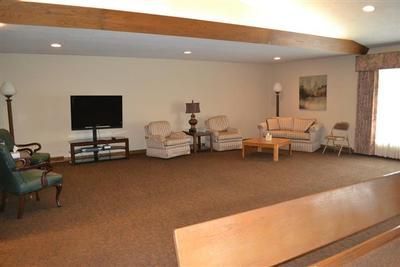 Spacious beige living room with TV, armchairs, sofa, coffee table, and large windows