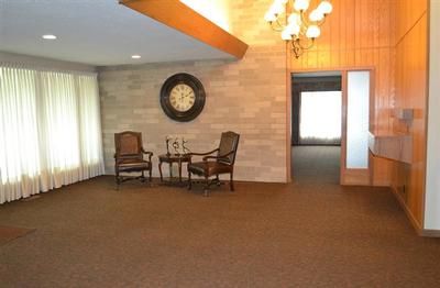 Empty carpeted lobby with chairs, wall clock, chandelier, and bright windows.