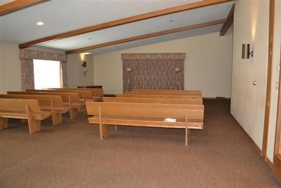 Empty church interior with wooden pews, tan carpet, and a small altar area at the front