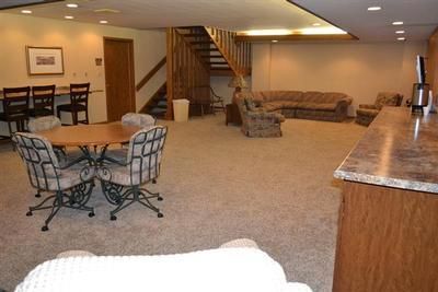Empty living room with carpet, sofas, dining table, and staircase near wood-paneled bar area