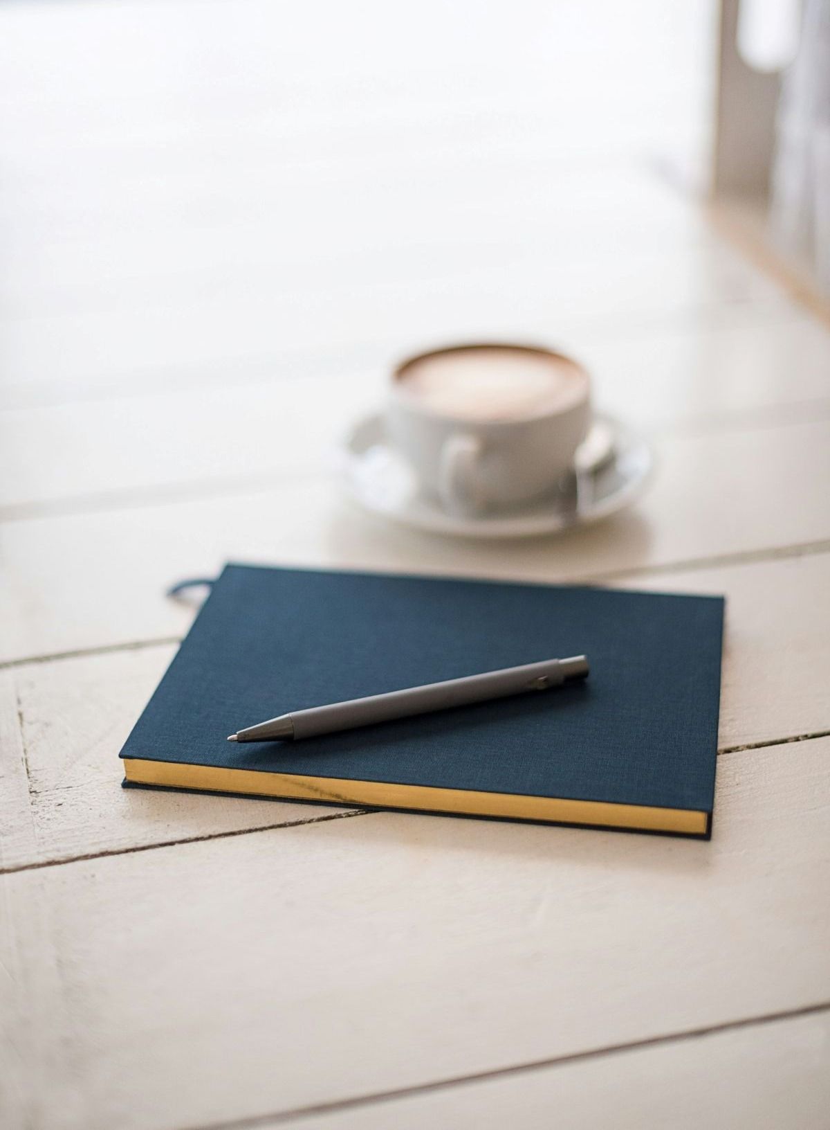 Blue notebook with a pen on a white table beside a cup of coffee