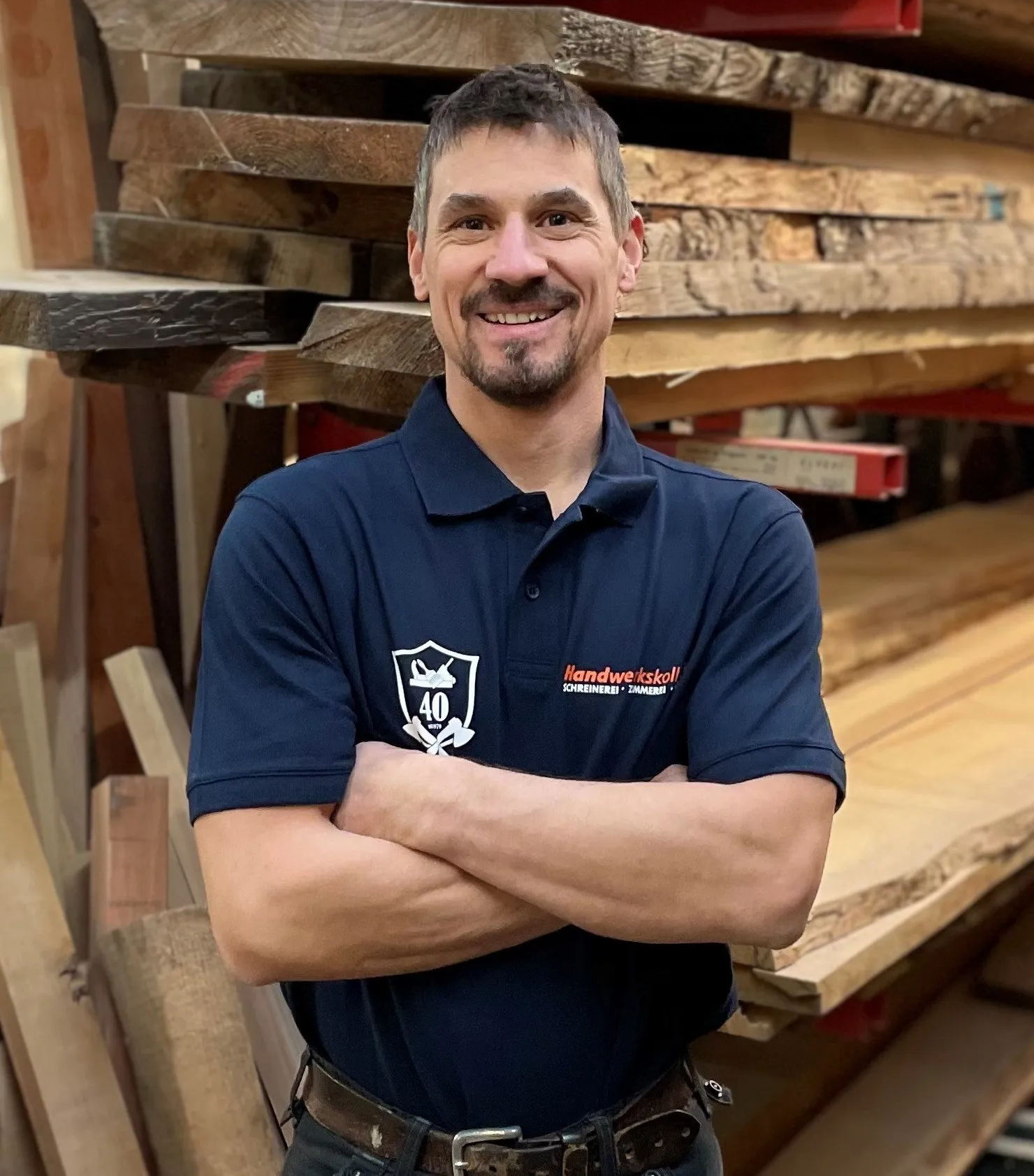 Ein Mann in einem blauen Hemd steht vor einem Holzstapel.