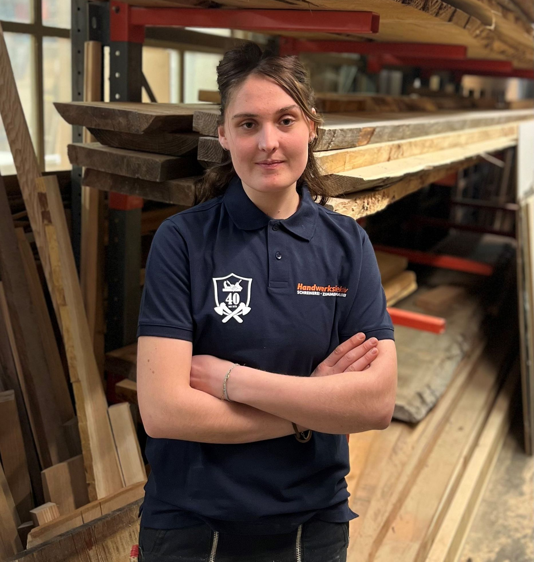 Eine Frau in einem blauen Hemd steht vor einem Holzstapel.