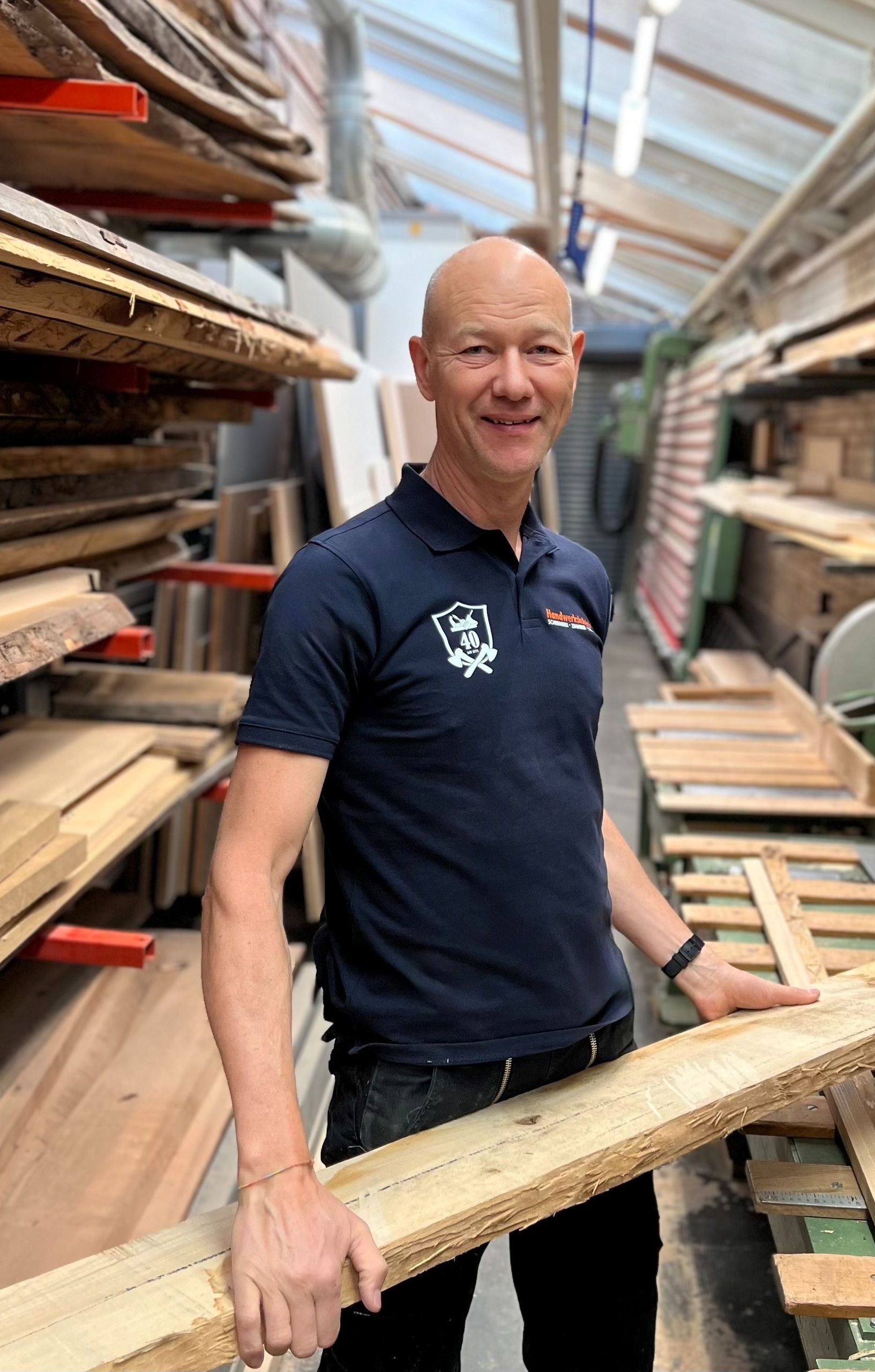 Ein Mann hält in einer Lagerhalle ein grosses Stück Holz.