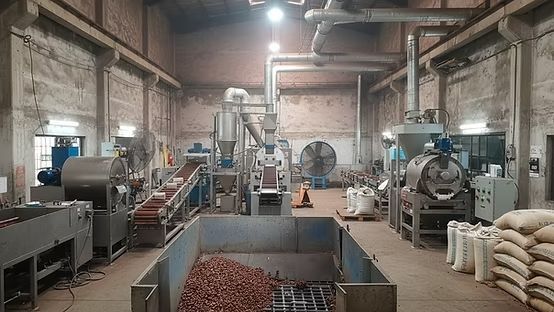 Nave industrial con maquinaria, contenedores de material marrón y sacos blancos apilados bajo techos altos