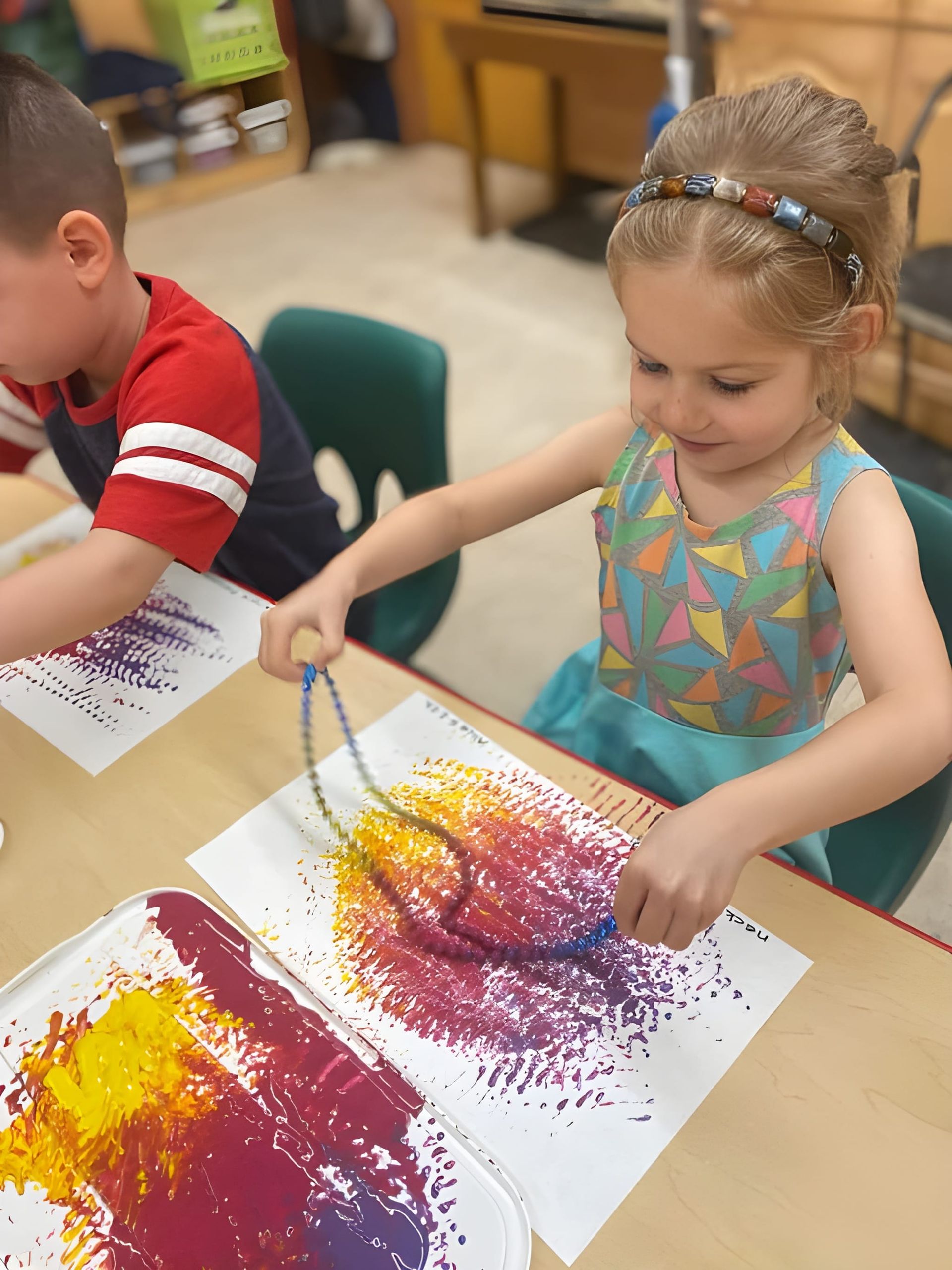A boy and a girl are sitting at a table playing with paint.