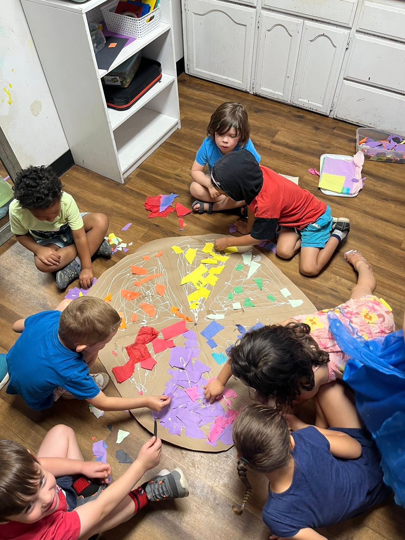 A group of children are sitting on the floor playing with paper.