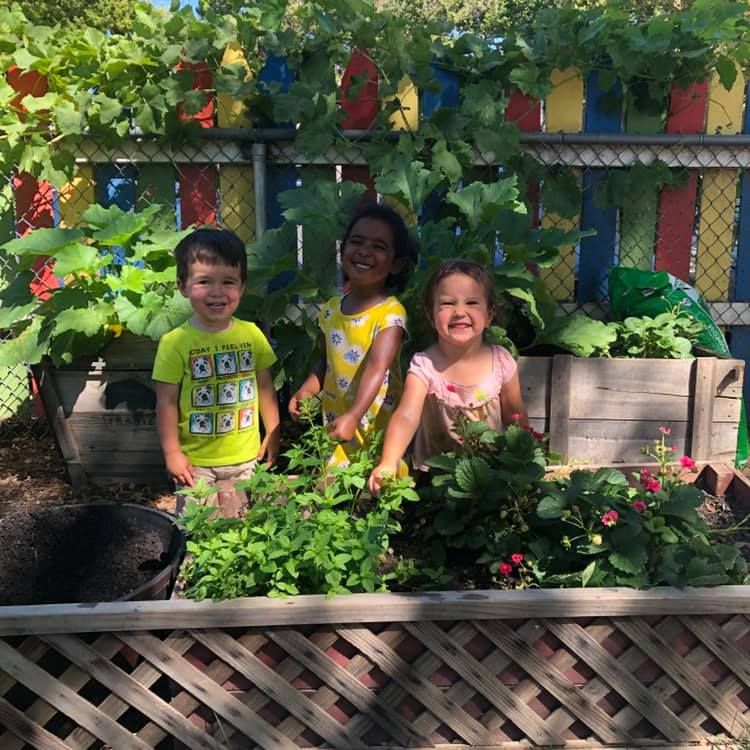 A boy and two girls are standing in a garden