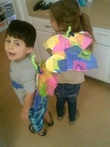 A boy and a girl are standing next to each other in a kitchen . the girl is wearing a butterfly costume.