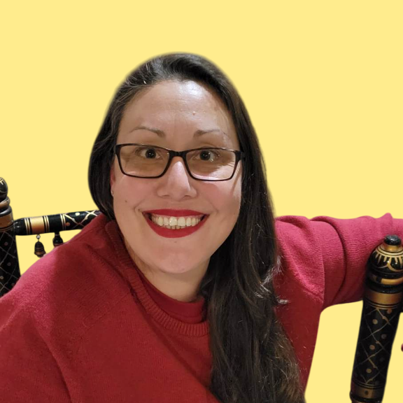 A woman wearing glasses and red lipstick smiles while sitting in a chair
