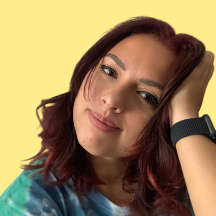 A woman with red hair is wearing a tie dye shirt and a watch.
