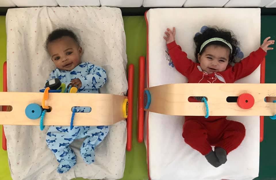 A boy and a girl are laying in cribs with their arms outstretched