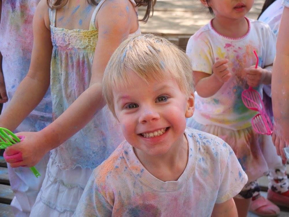 A young boy is smiling in front of a group of children covered in paint.