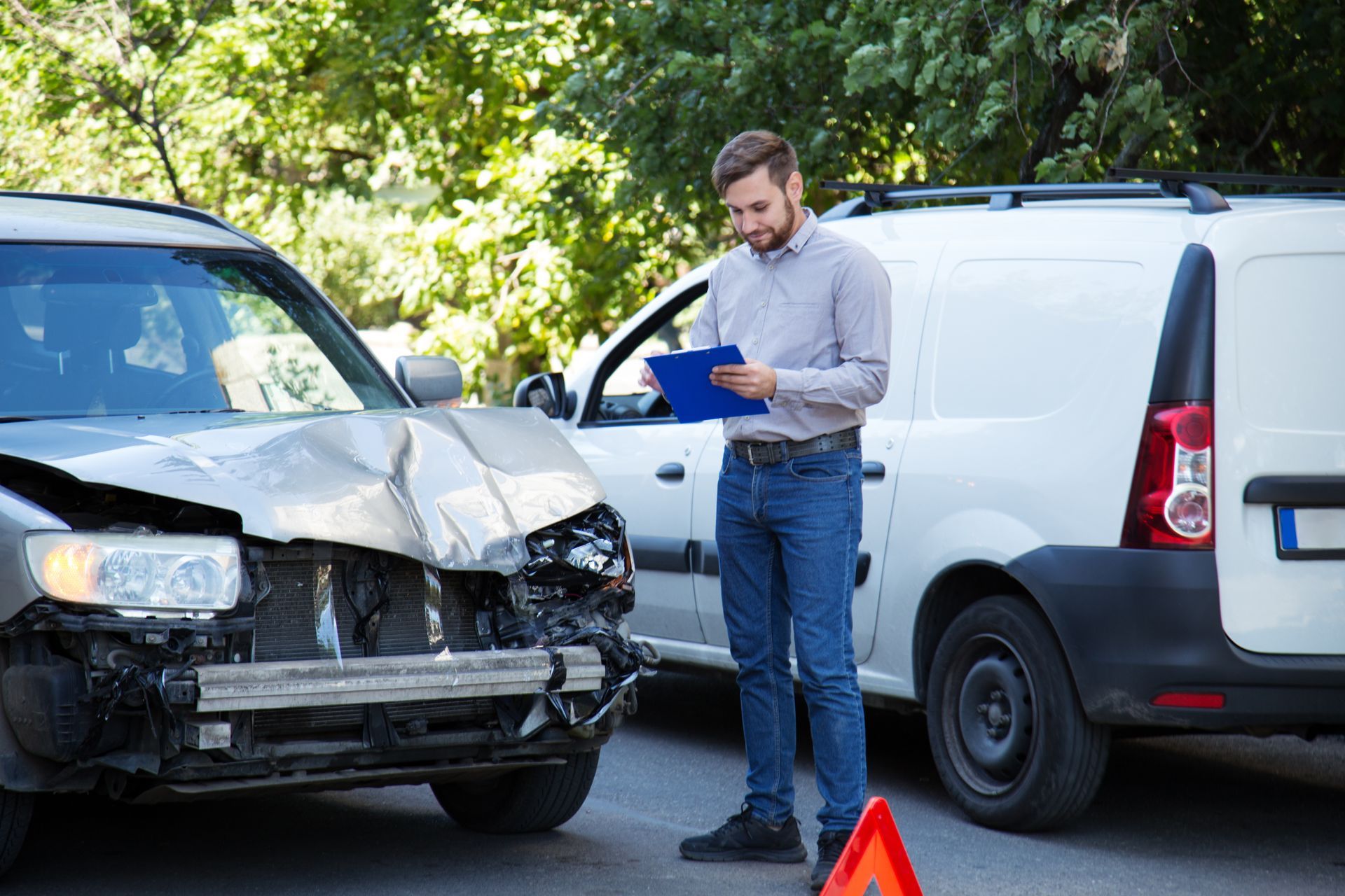 Man in jeans and a shirt inspecting two damaged vehicles after a car accident.