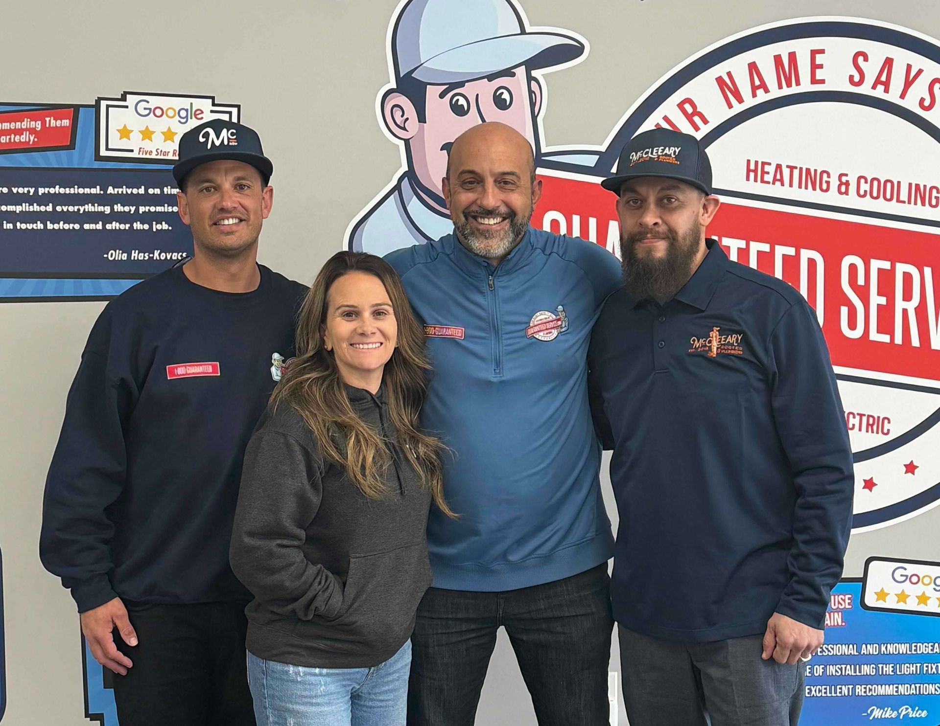 Four smiling staff members stand indoors in front of a heating and cooling service sign.