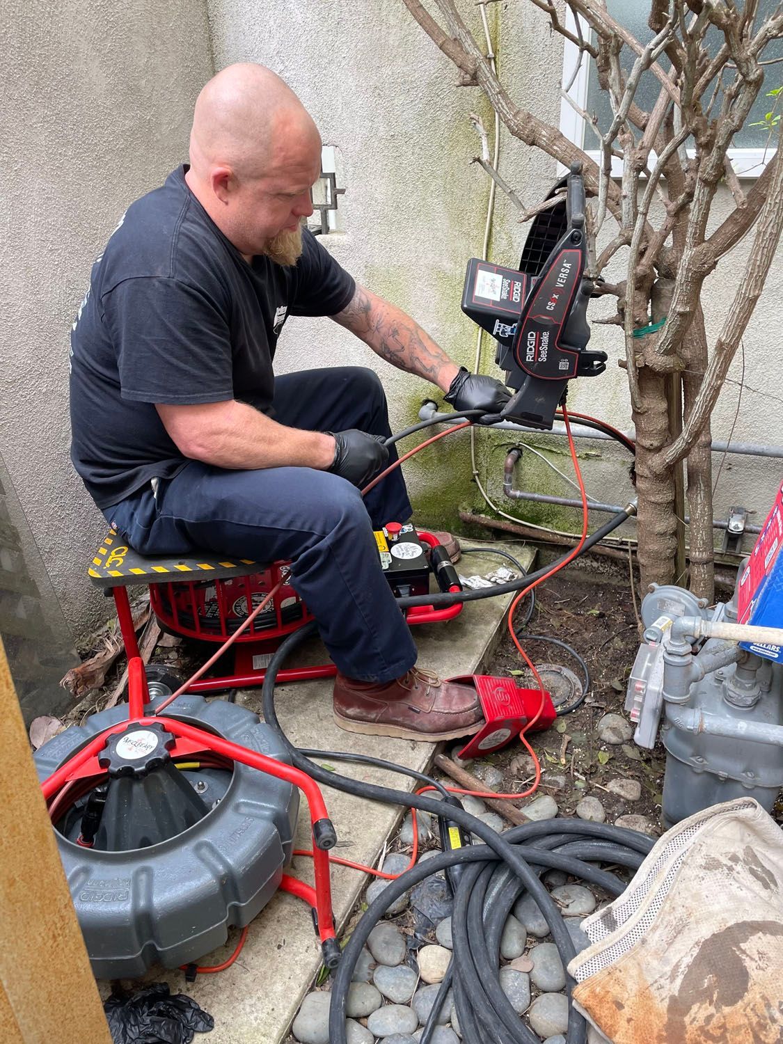 Plumber using a drain snake in a utility area beside pipes, cables, and tools