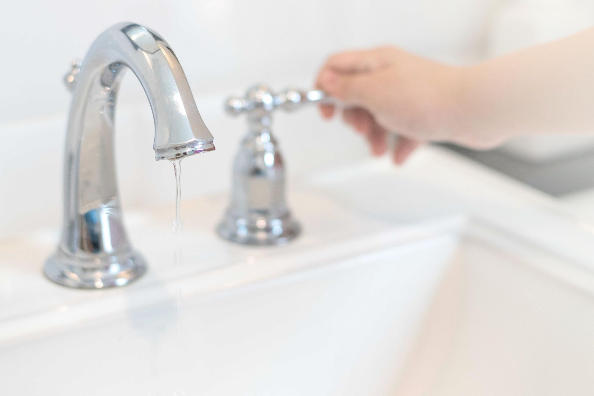 Hand turning on a silver bathroom faucet over a white sink