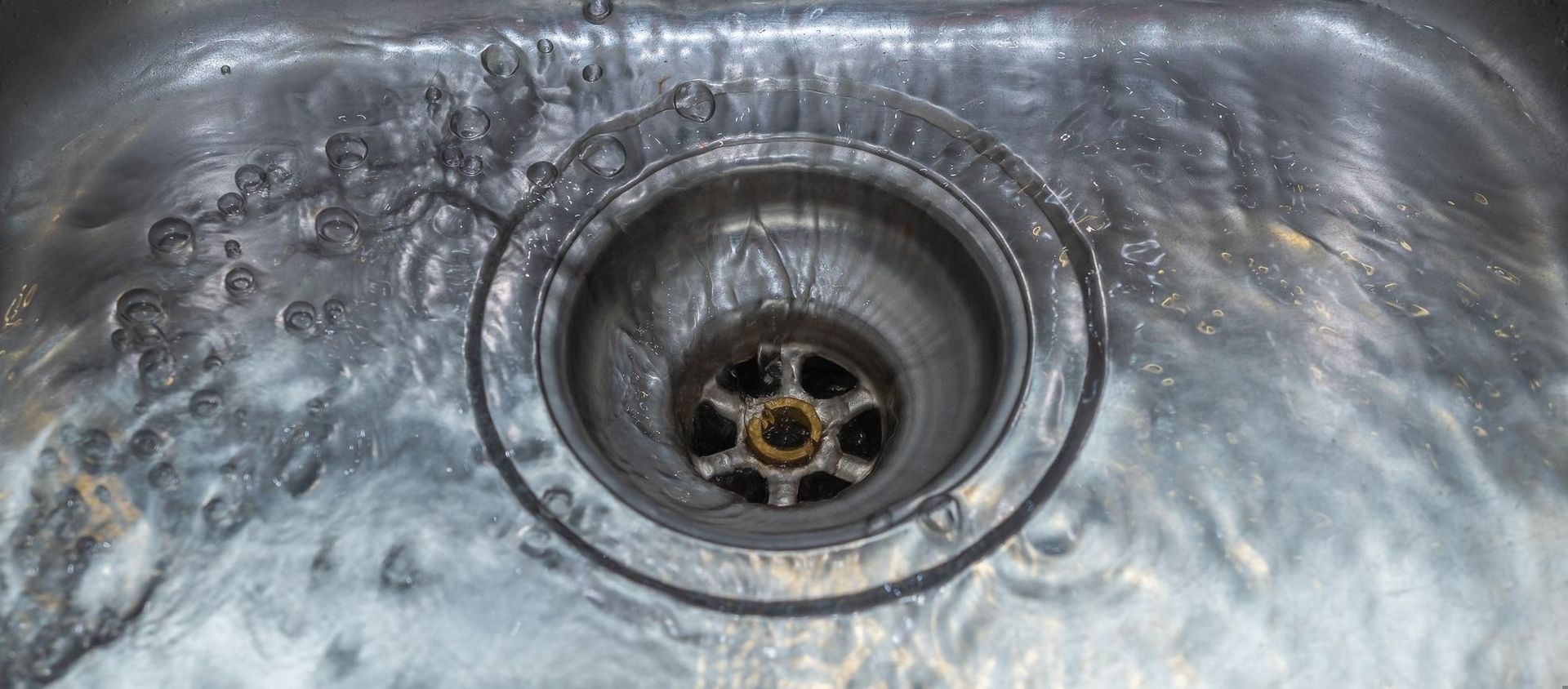 Stainless steel sink with a metal drain and visible grime around the basin
