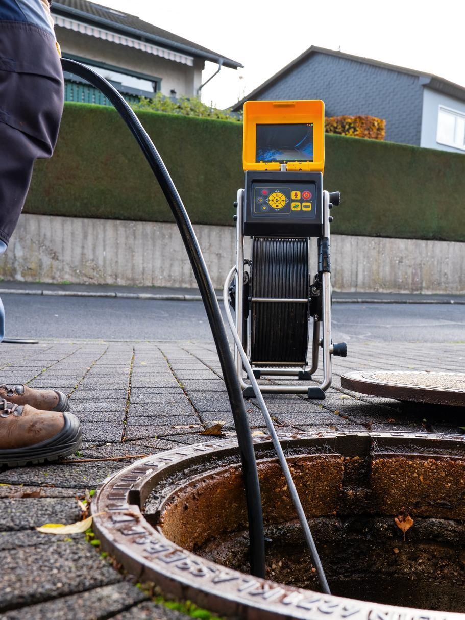 An orange-and-black sewer inspection camera lowered into an open manhole on a residential street.