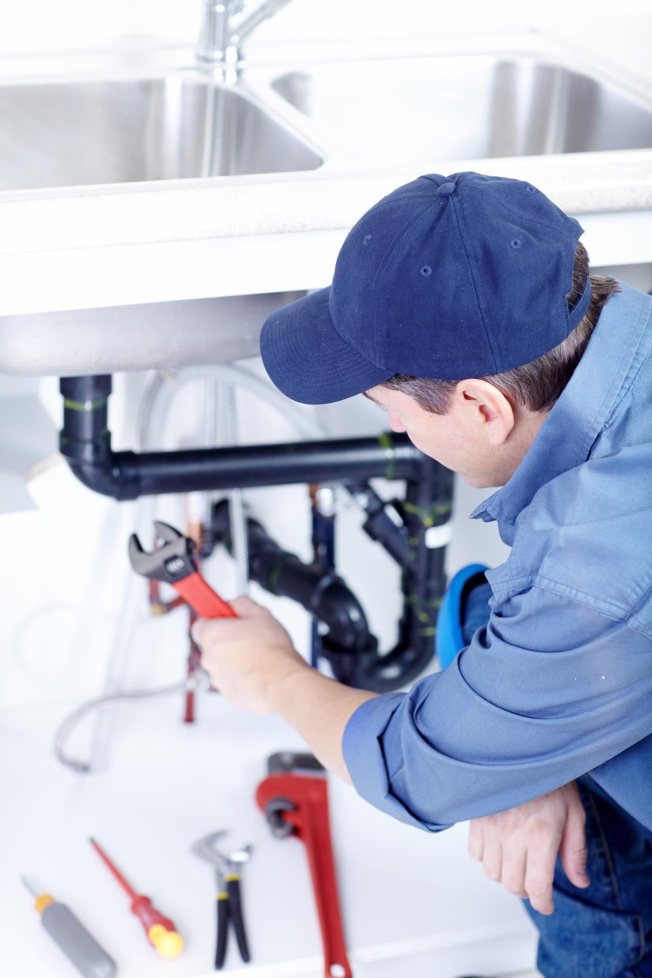 Plumber working under a sink with tools, tightening pipes beneath a stainless steel countertop