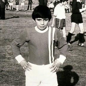 A young boy is standing on a soccer field with his hands on his hips.
