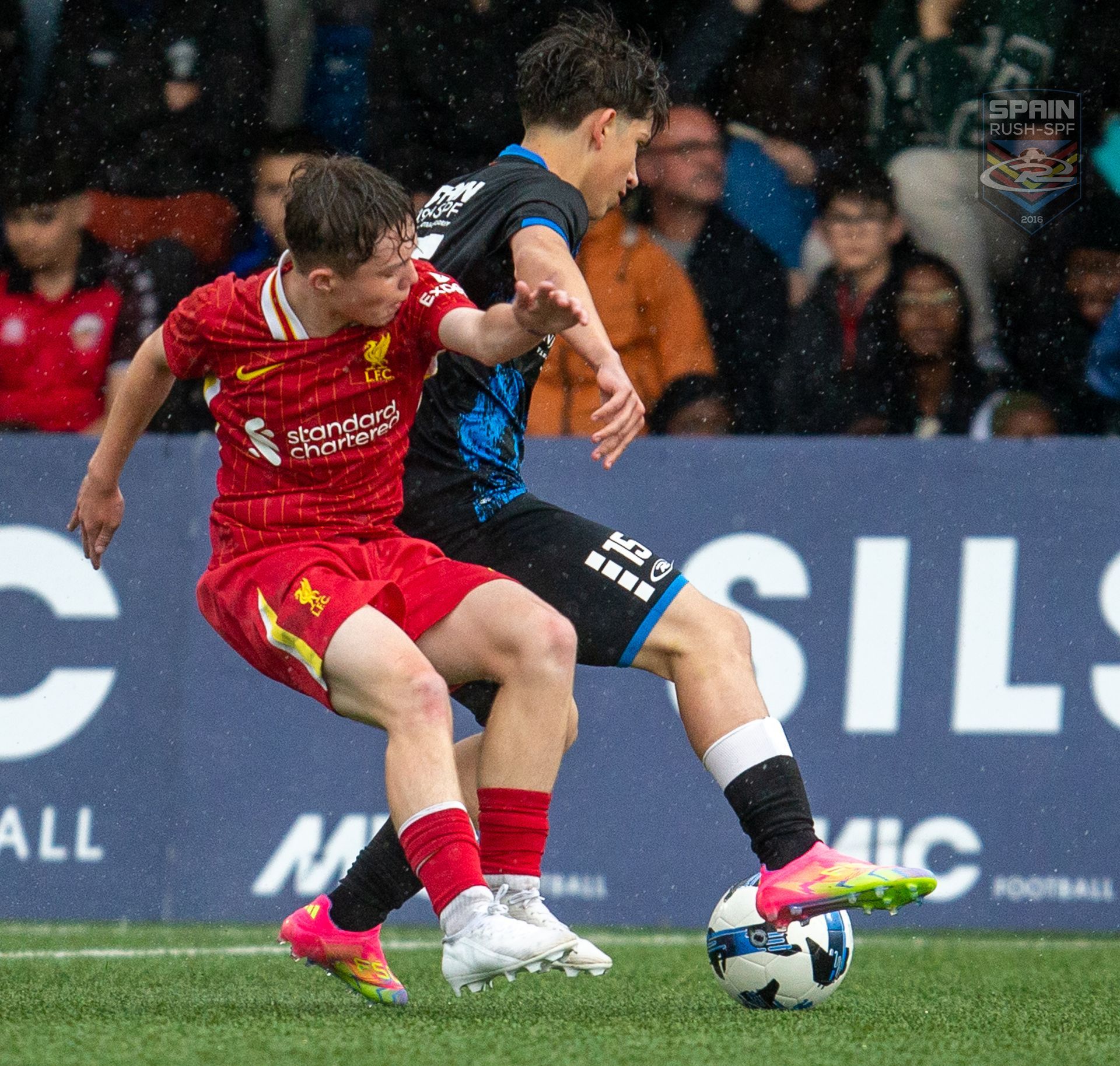 Two soccer players are fighting for the ball in front of a sign that says sils