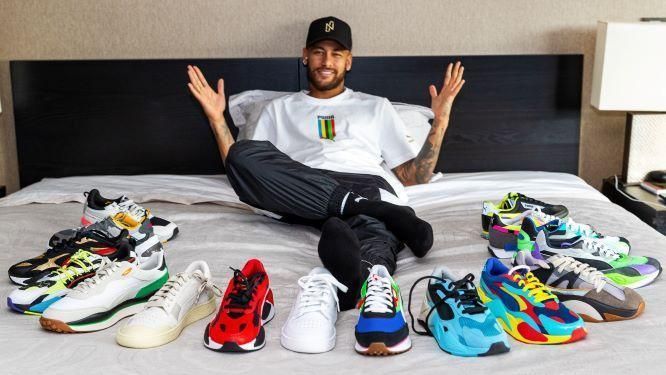 A man is sitting on a bed with a bunch of shoes on it.