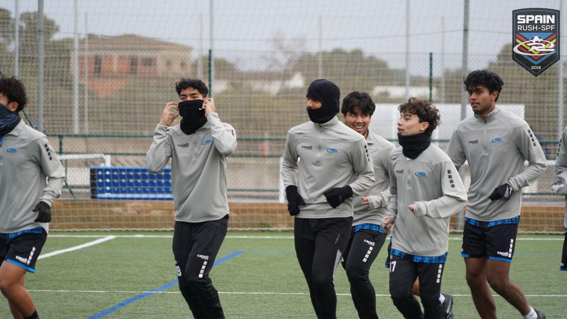 A group of young men wearing face masks are running on a soccer field.