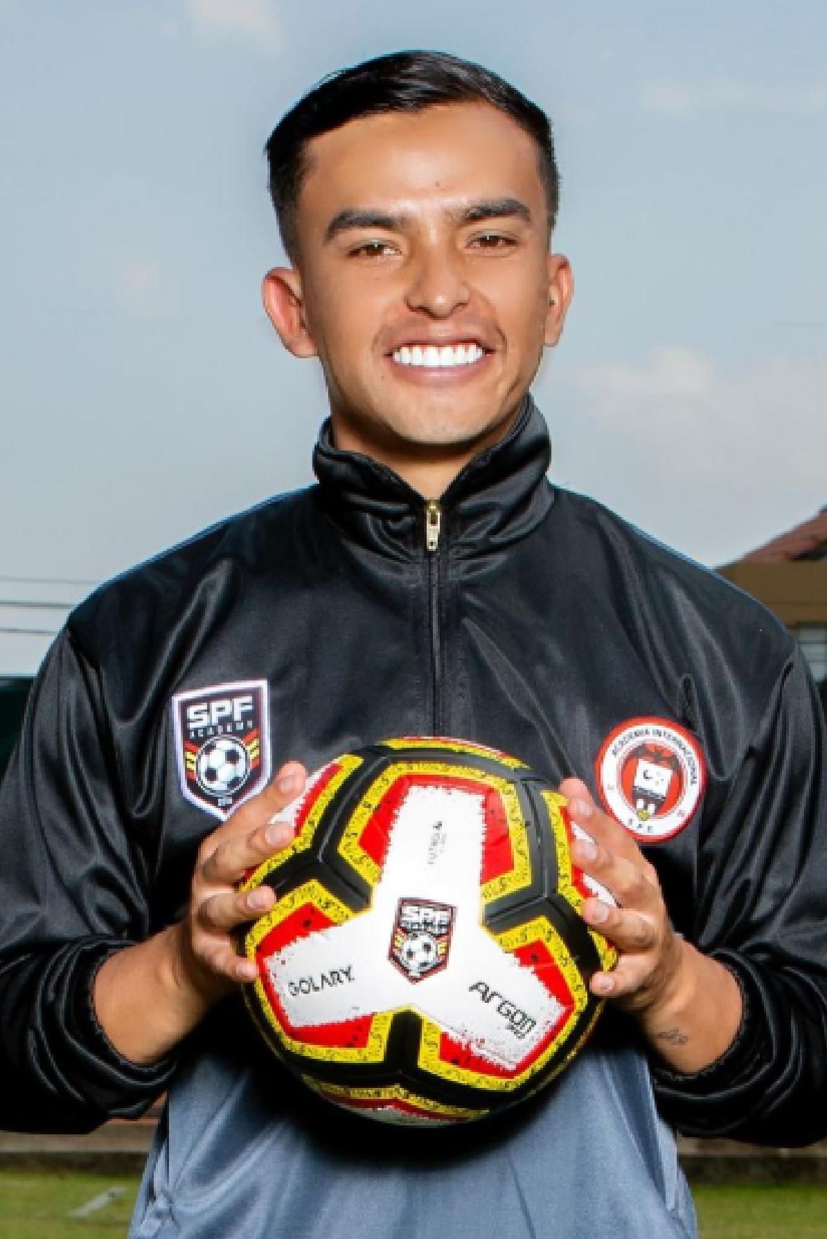 Juan Felipe Rodriguez in a black jacket is holding a soccer ball.