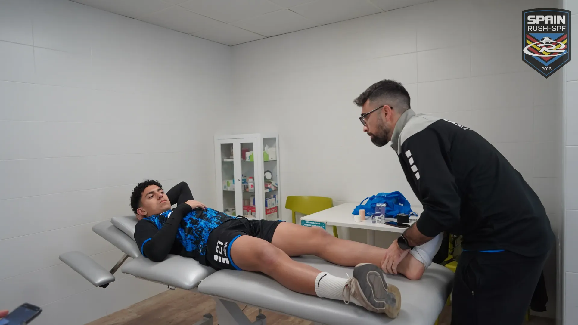 A man is putting a bandage on a soccer player 's leg.