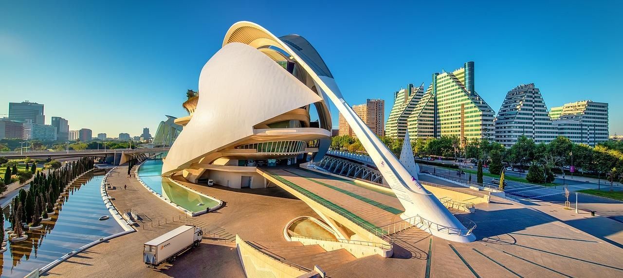 A large white building is sitting next to a river in a city.