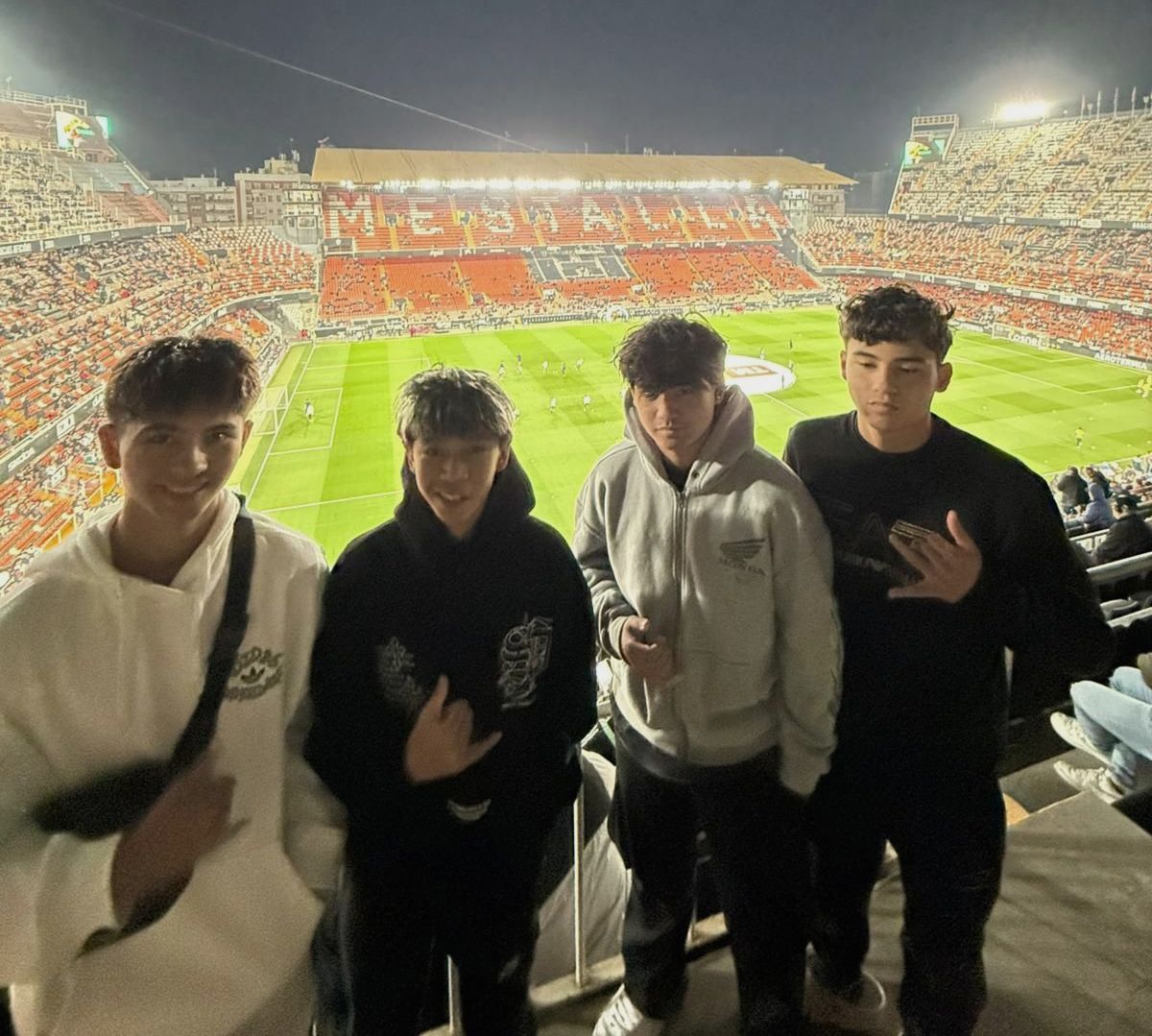 A group of young men are standing in front of a stadium at night.