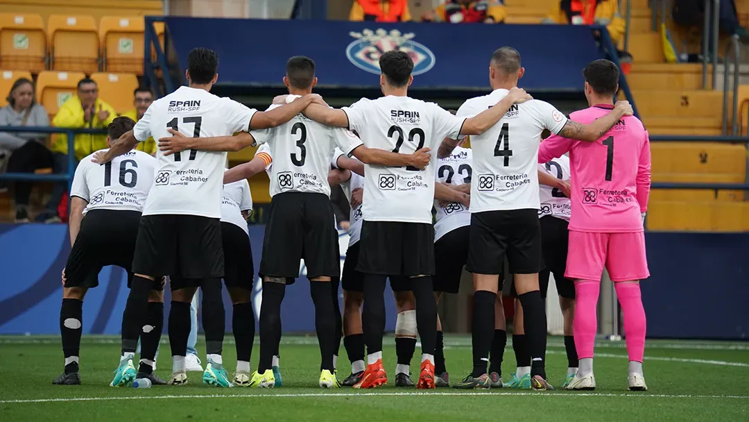 A group of soccer players are standing in a huddle on the field.