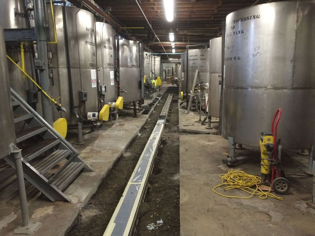 Rows of large stainless steel tanks in a dimly lit industrial space; a drainage channel runs along the floor.