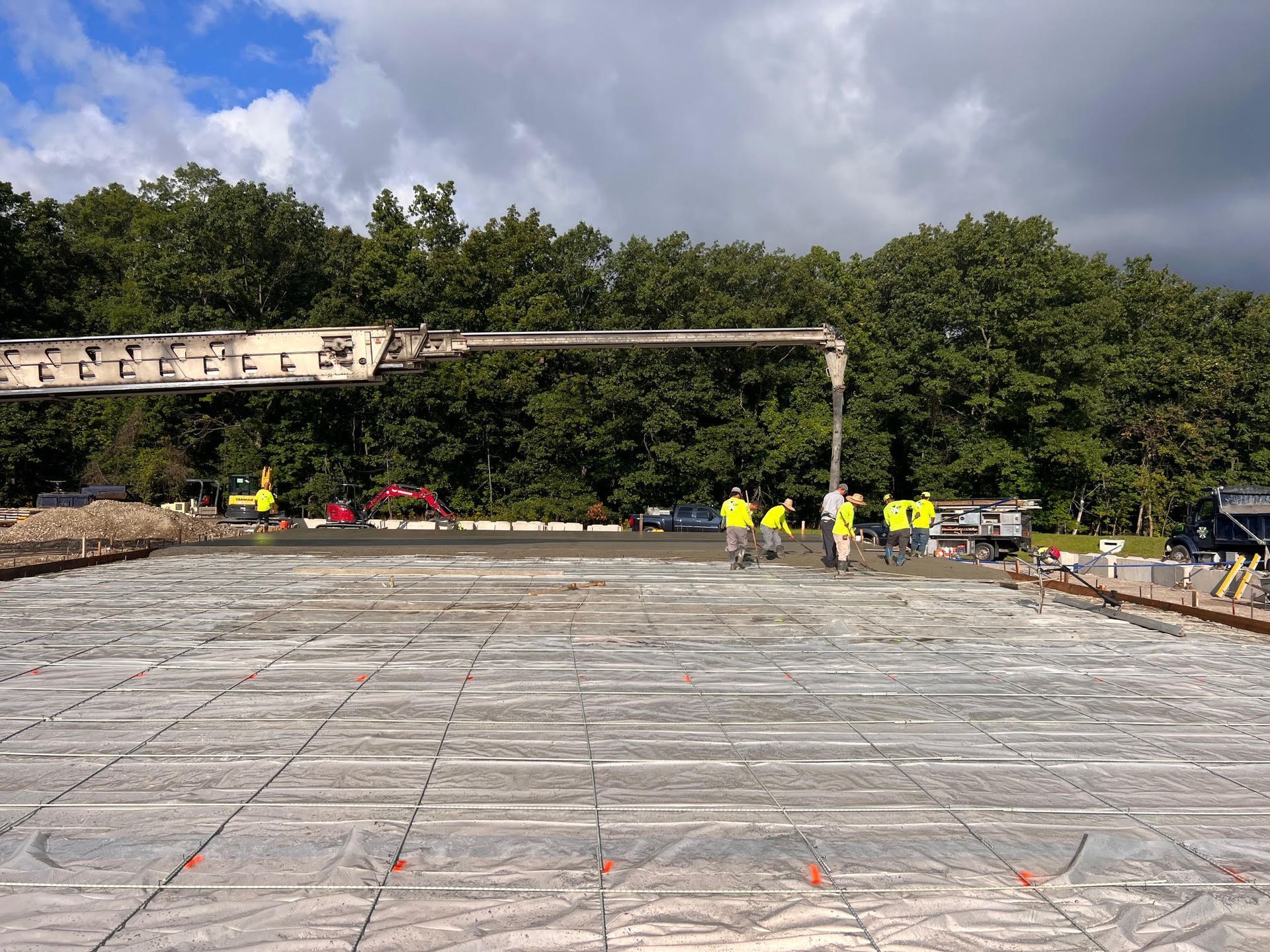 Concrete being poured onto a grid with workers in yellow vests; trees in the background.