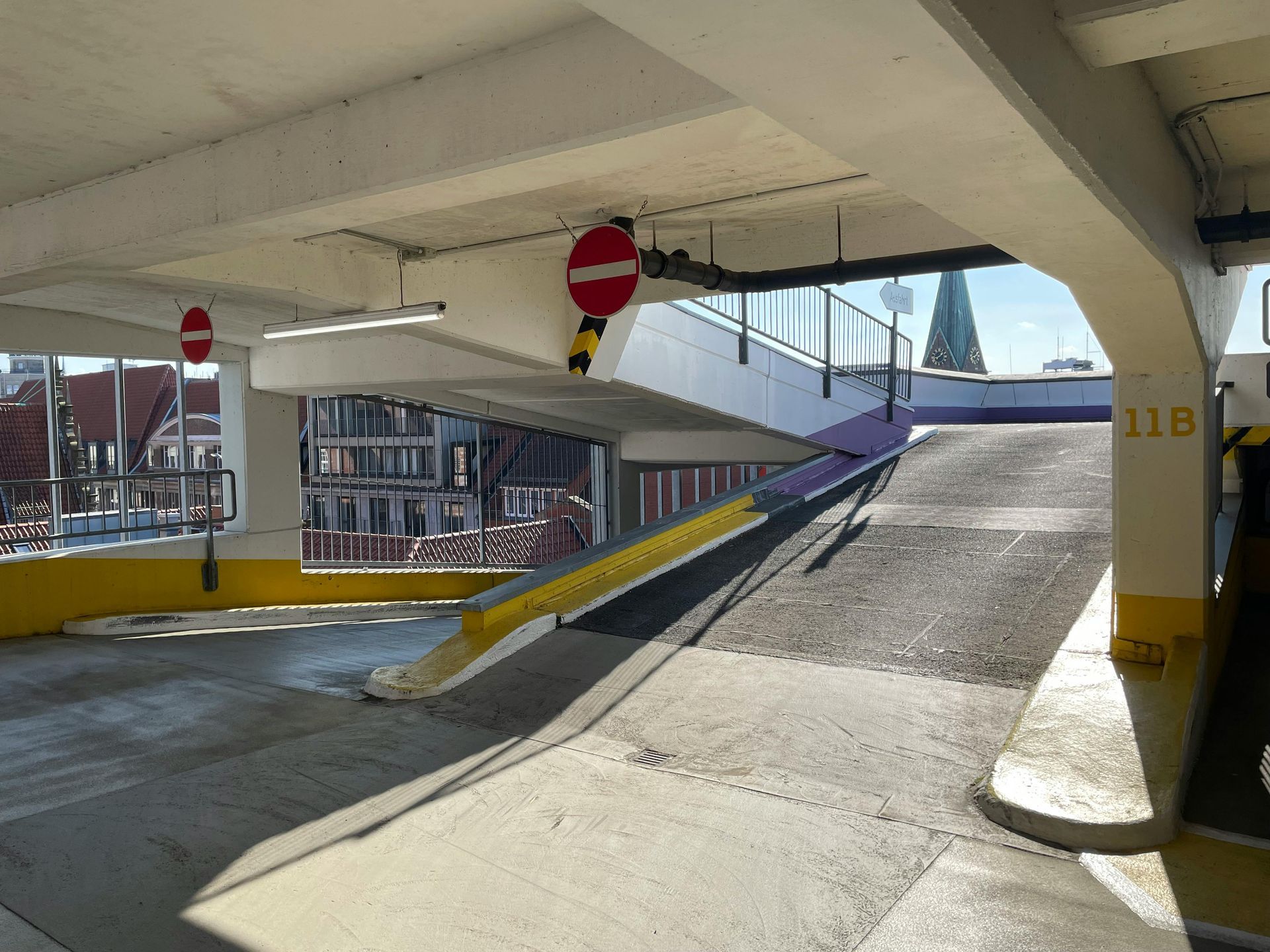 Covered parking ramp with a sloped concrete driveway and red no-entry signs, viewed from under a structure
