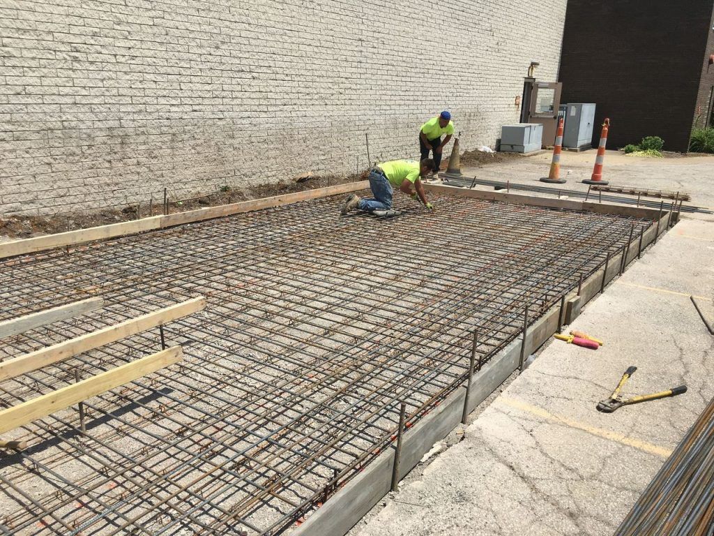 Construction workers pouring concrete, reinforcing rebar grid in an outdoor setting.