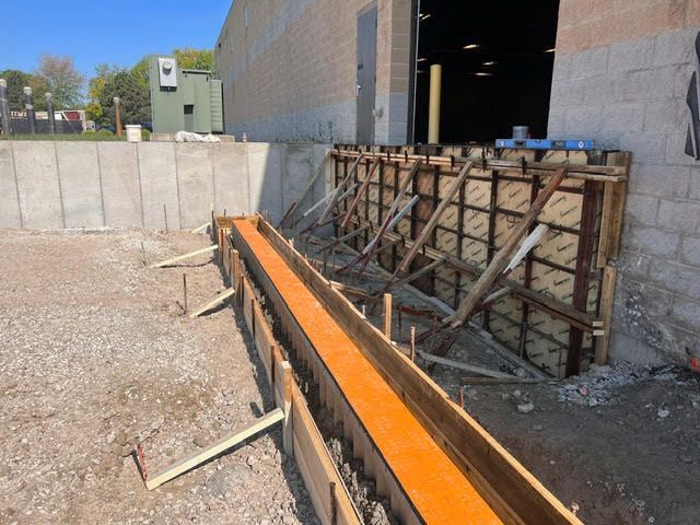 Construction site with wooden forms for concrete along a building, dirt ground.