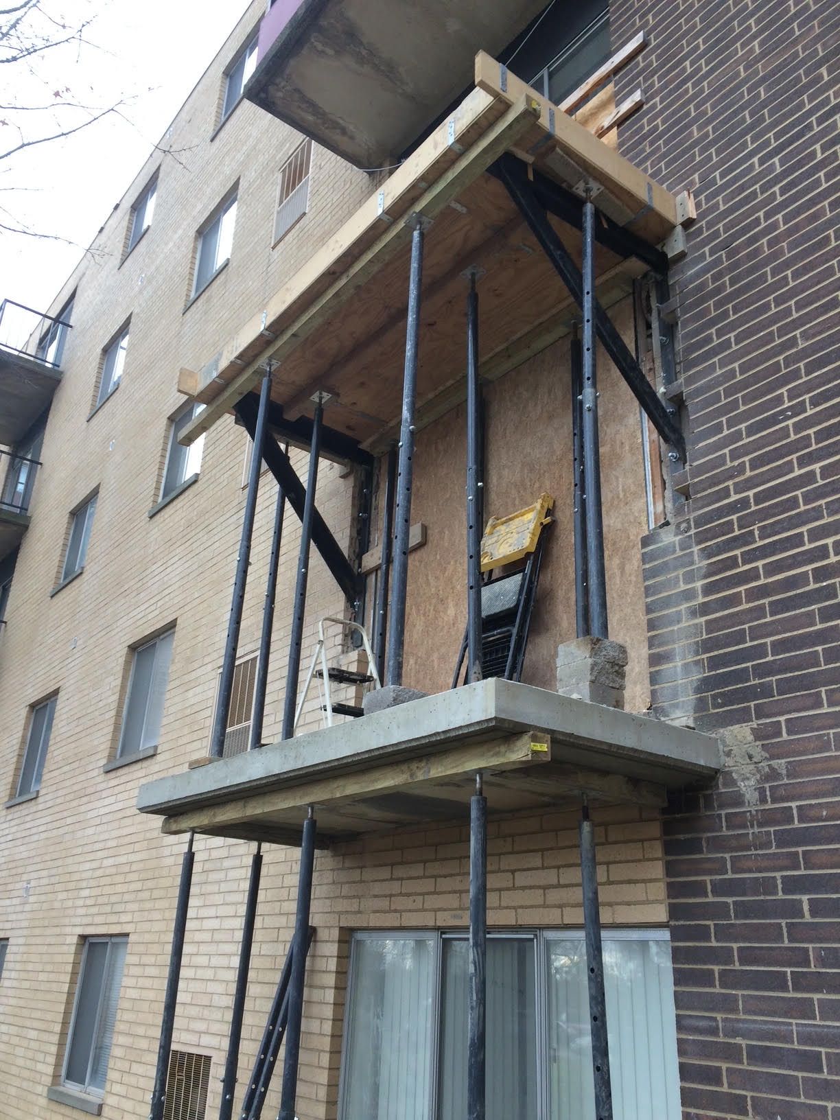 Apartment balcony undergoing repairs, supported by black metal scaffolding.