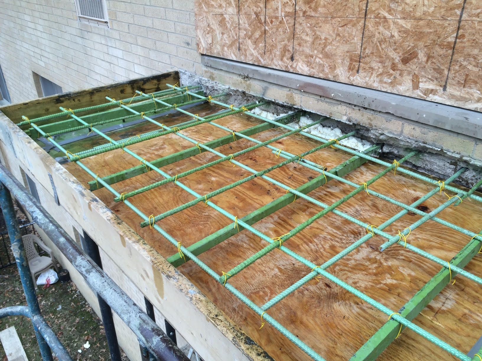 Green rebar grid on plywood formwork, likely for a concrete pour on a building exterior.