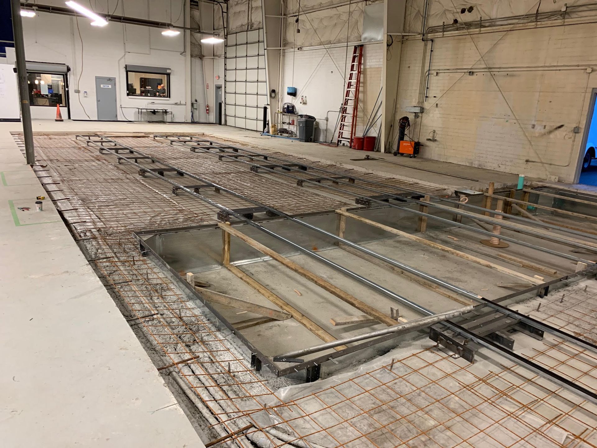 Construction site: exposed rebar grid, open pits, and steel framework on a concrete floor inside a large building.
