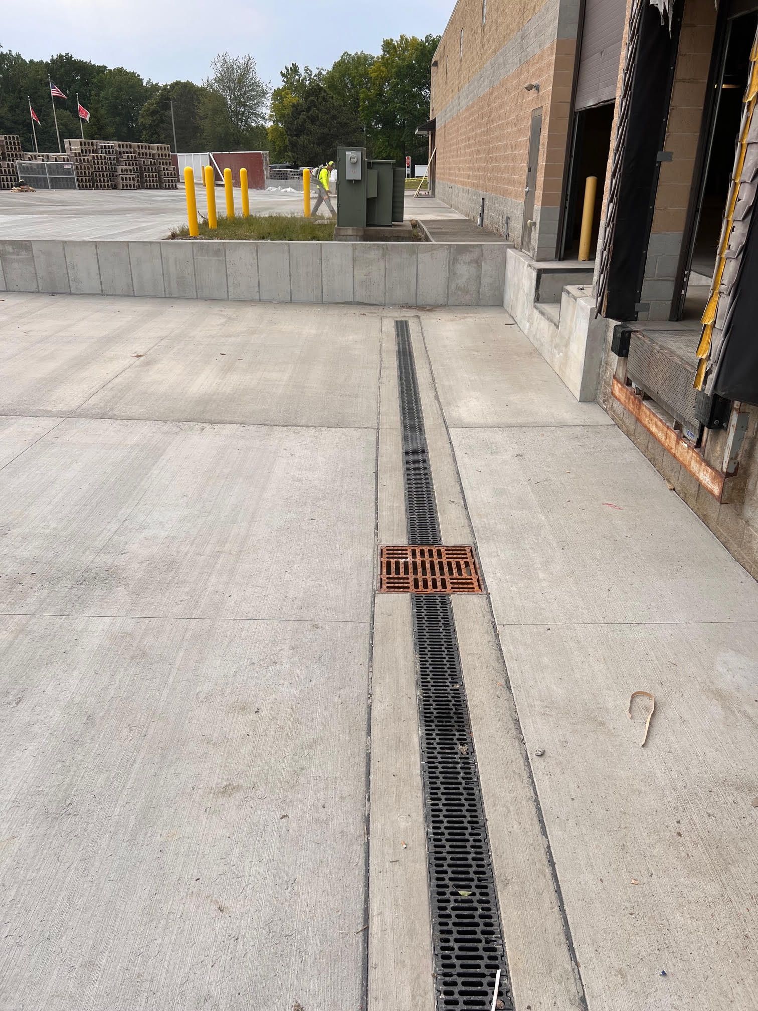Concrete loading dock with a long metal drain. Yellow bollards and brick building in the background.