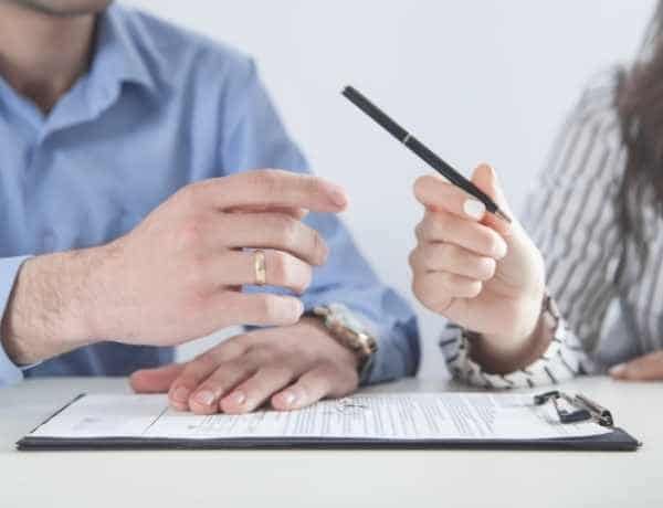 A man and a woman are sitting at a table with a clipboard and a pen.