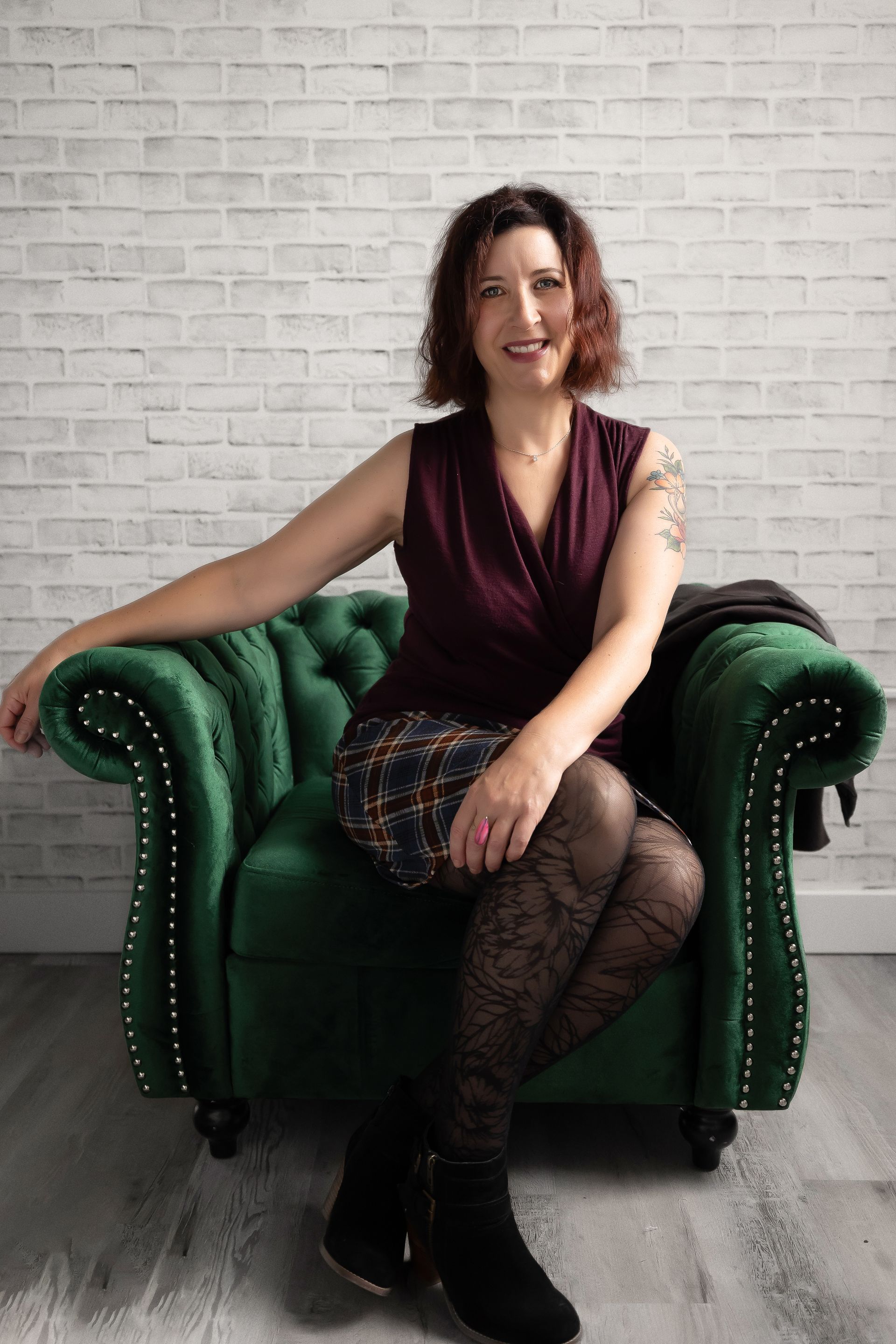 A woman is sitting in a green chair in front of a white brick wall.