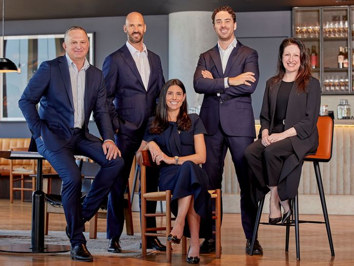 Five people, three men and two women, pose in a business setting. They are wearing suits, smiling, and looking at the camera.